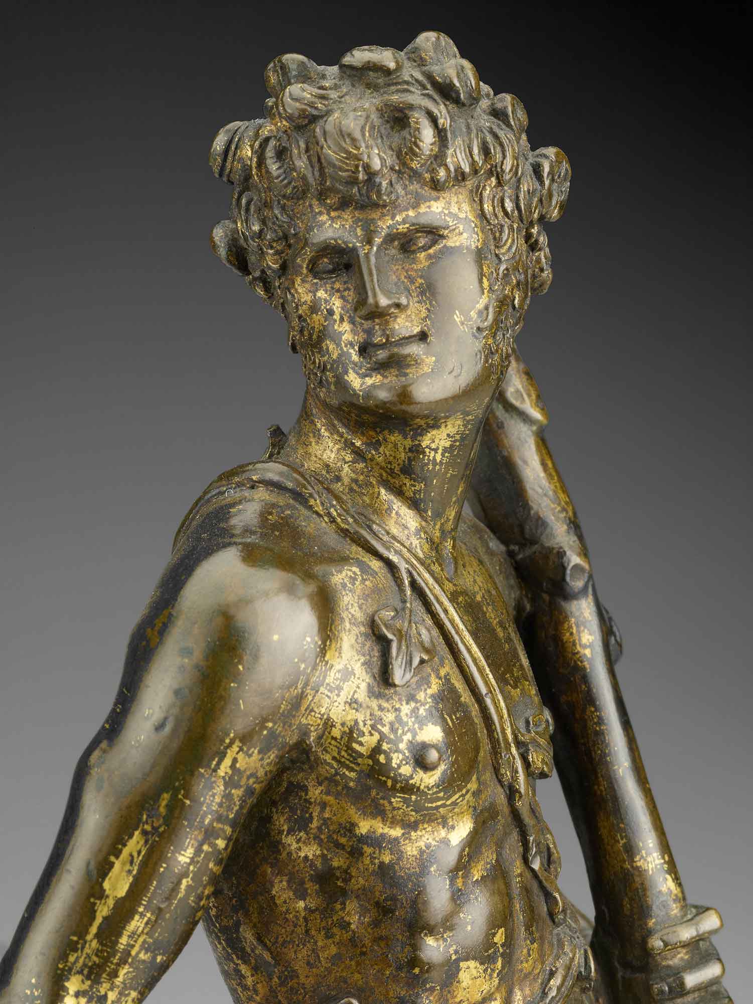 closeup of brozne statuette of young man holding club