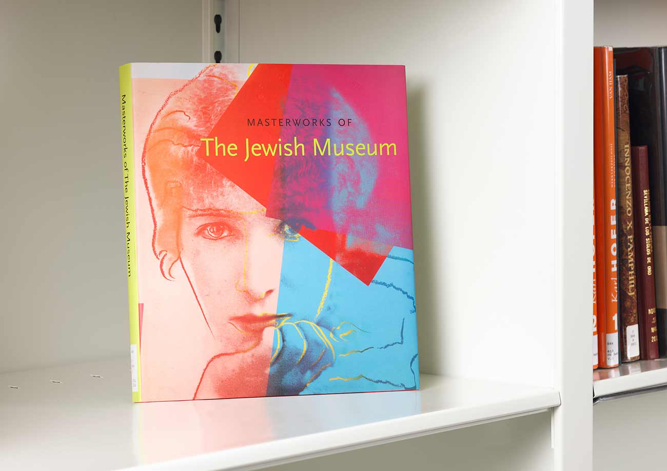 Book on a white shelf whose cover features a Pop art portrait of a woman's face with her hand at her chin