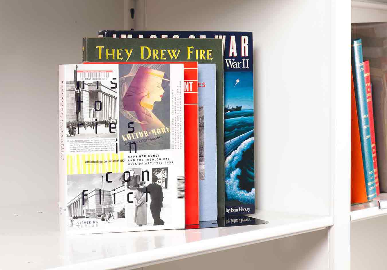 Five books on art and World War Two stacked on a white shelf. The front book cover features clippings of Nazi-era art images.