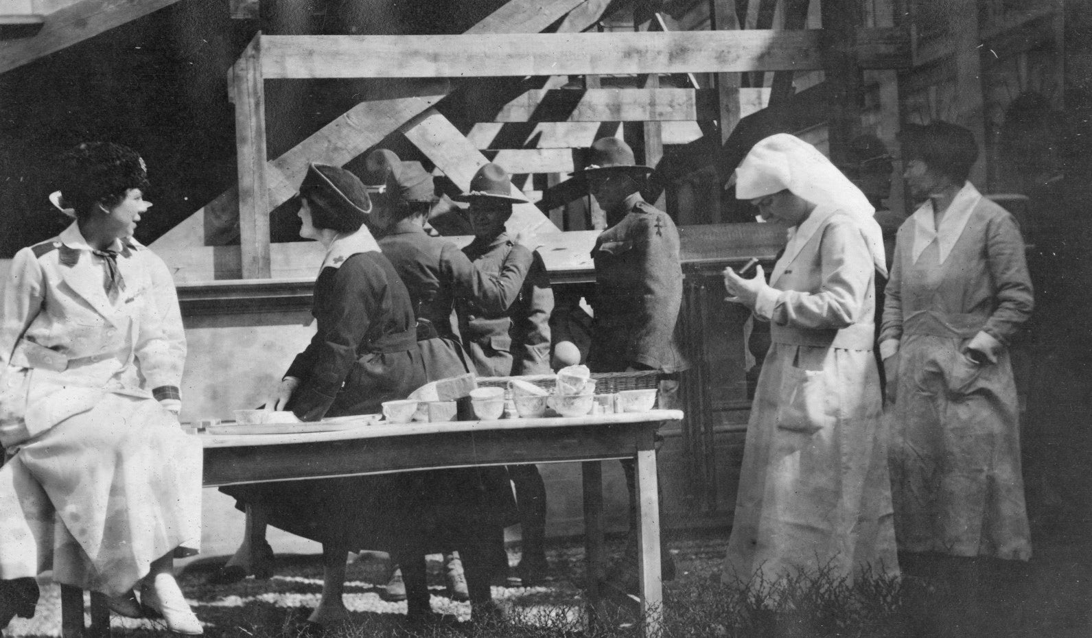 Soldiers and Red Cross volunteers in front of the base of a wooden viewing stand.