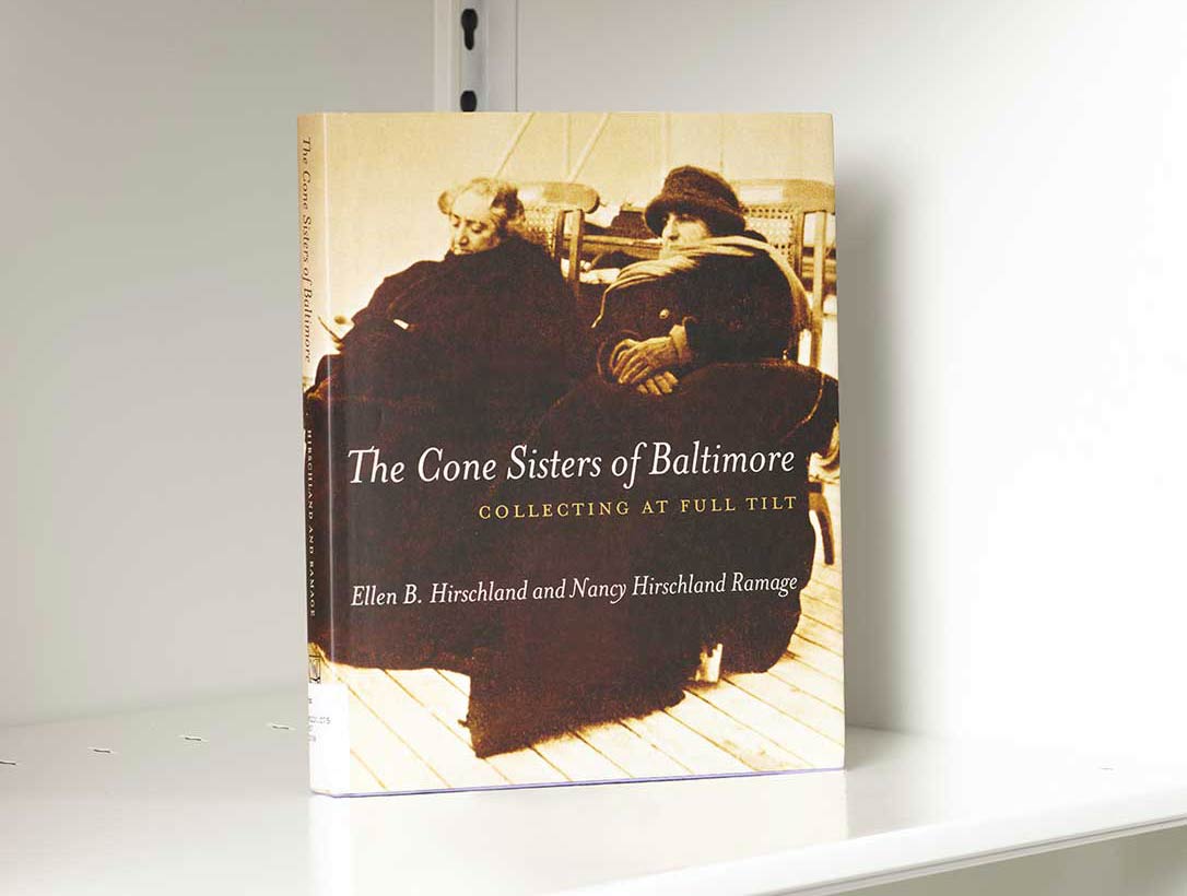 Book on a white shelf whose cover features a photo of two seated women in large dark coats and hats