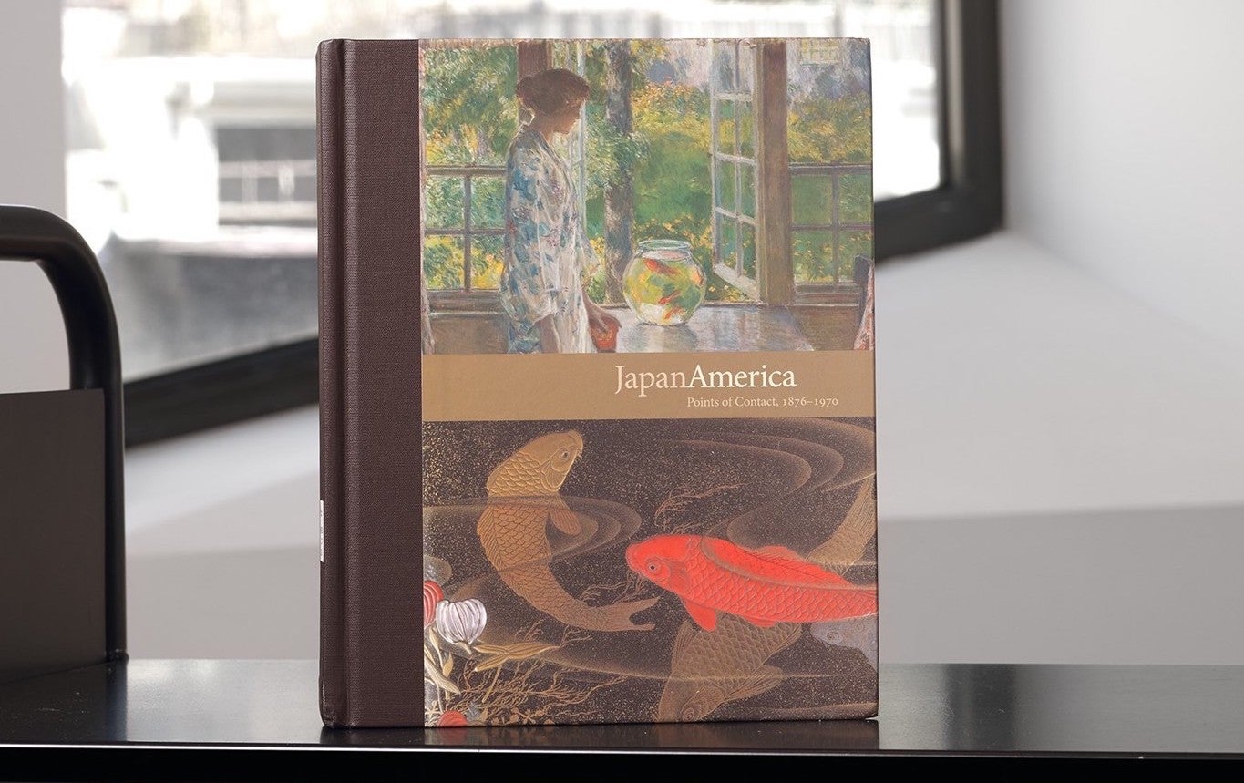 Book with details of a Japanese-inspired Western painting and a Japanese artwork of fishes on its cover on a library cart in front of a window