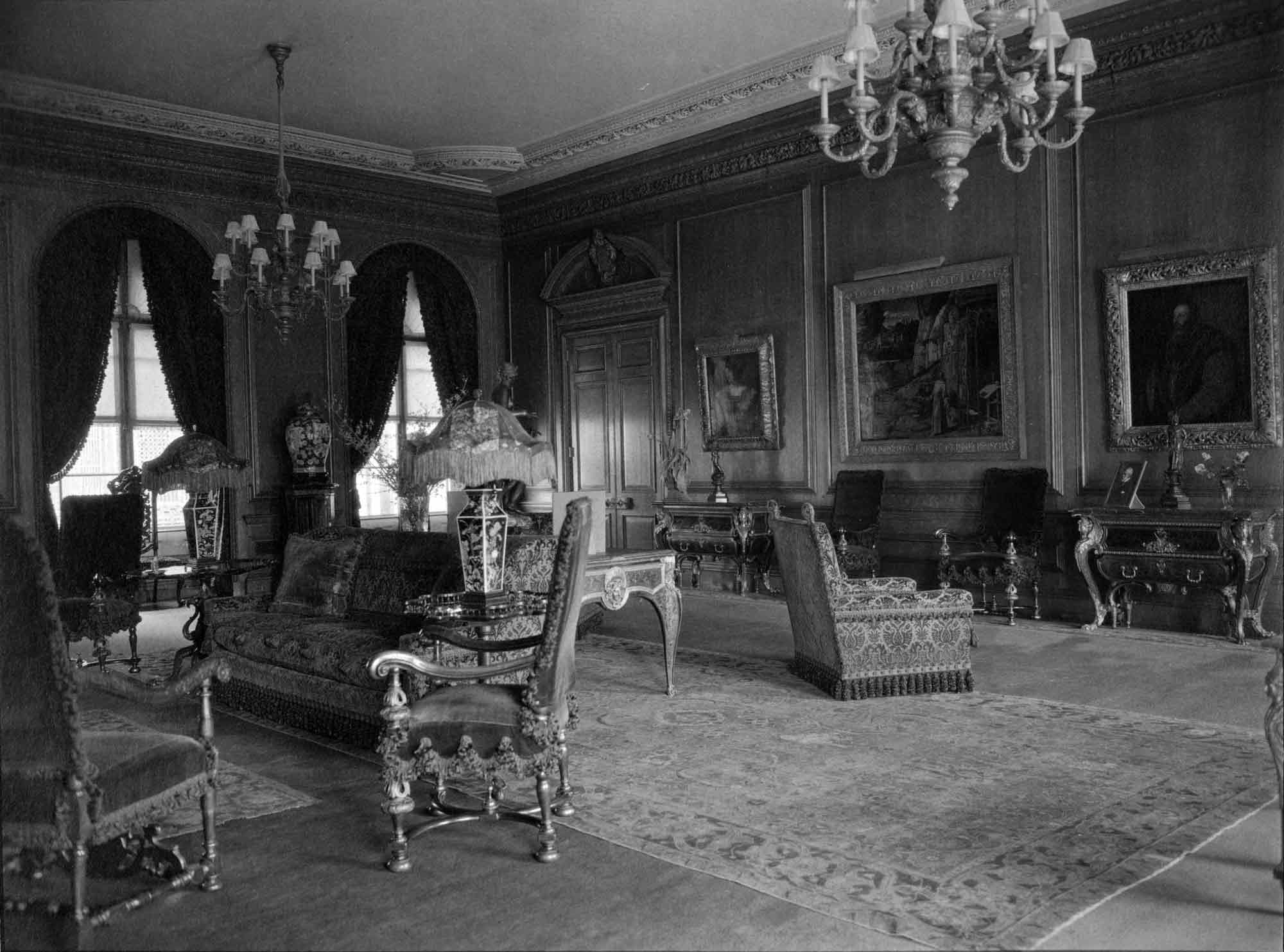 Room of a mansion with three large paintings, furniture, and chandeliers