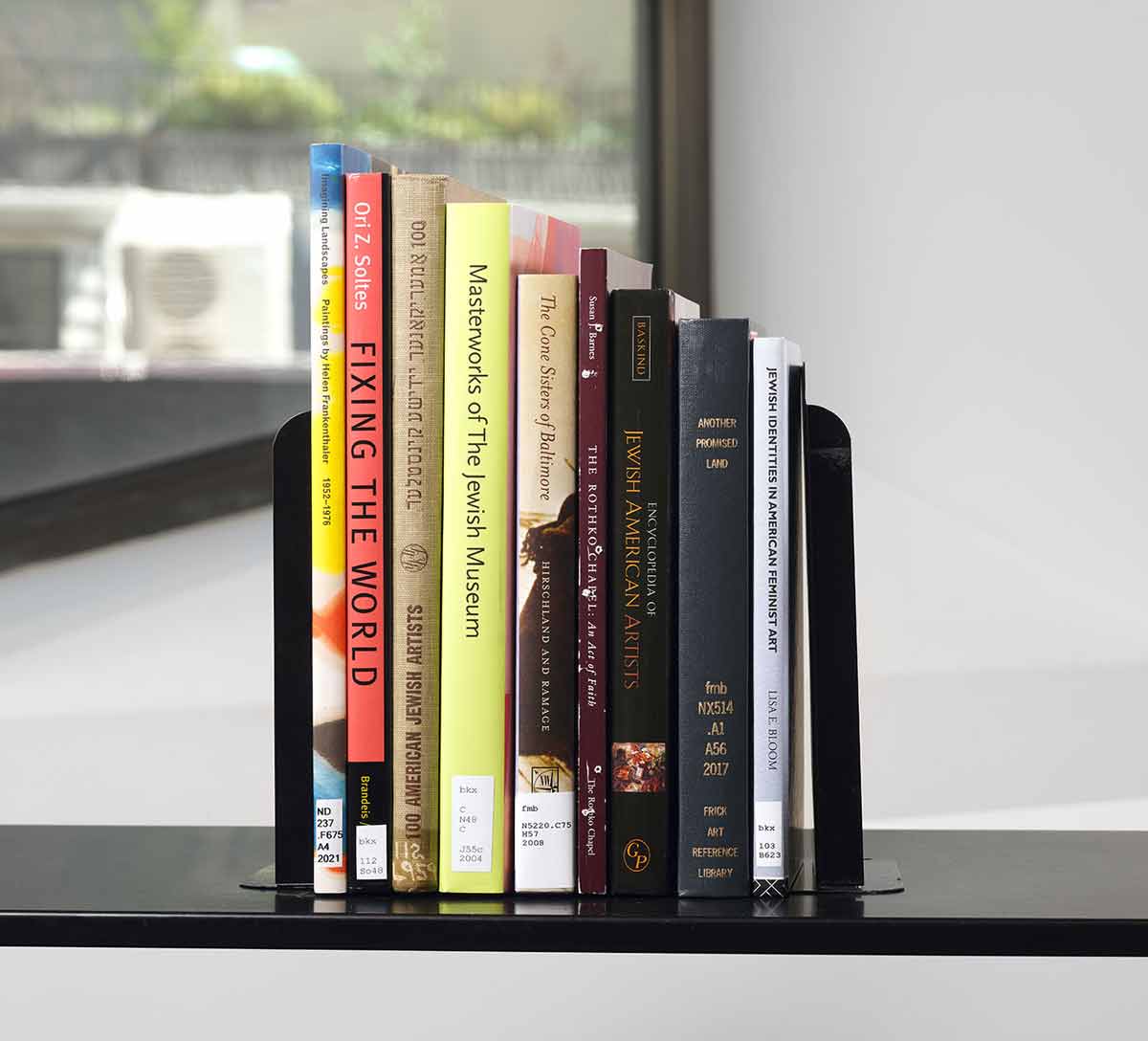 Stack of nine books on a black cart in front of a window