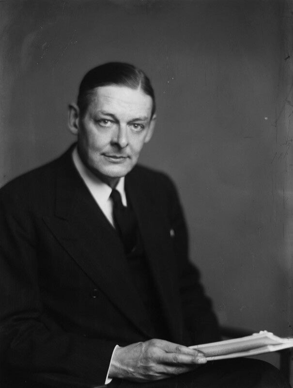 Photograph of a seated man wearing a suit, holding papers and looking out at the viewer