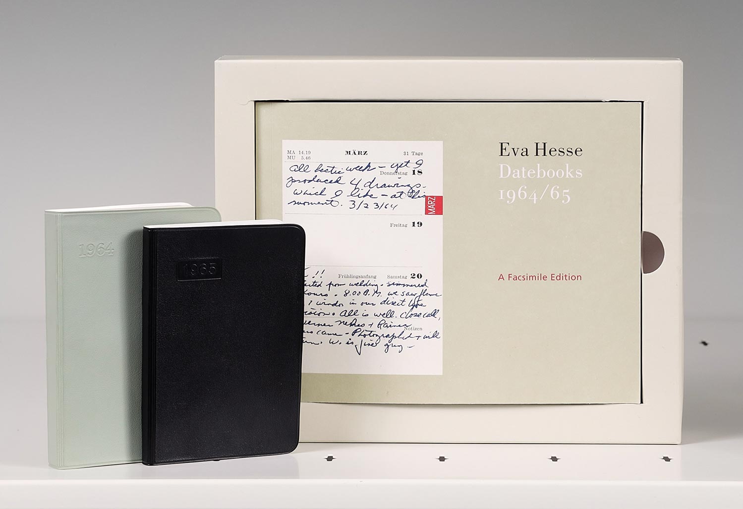 A horizontal book in a box next to two smaller books, one black and one green