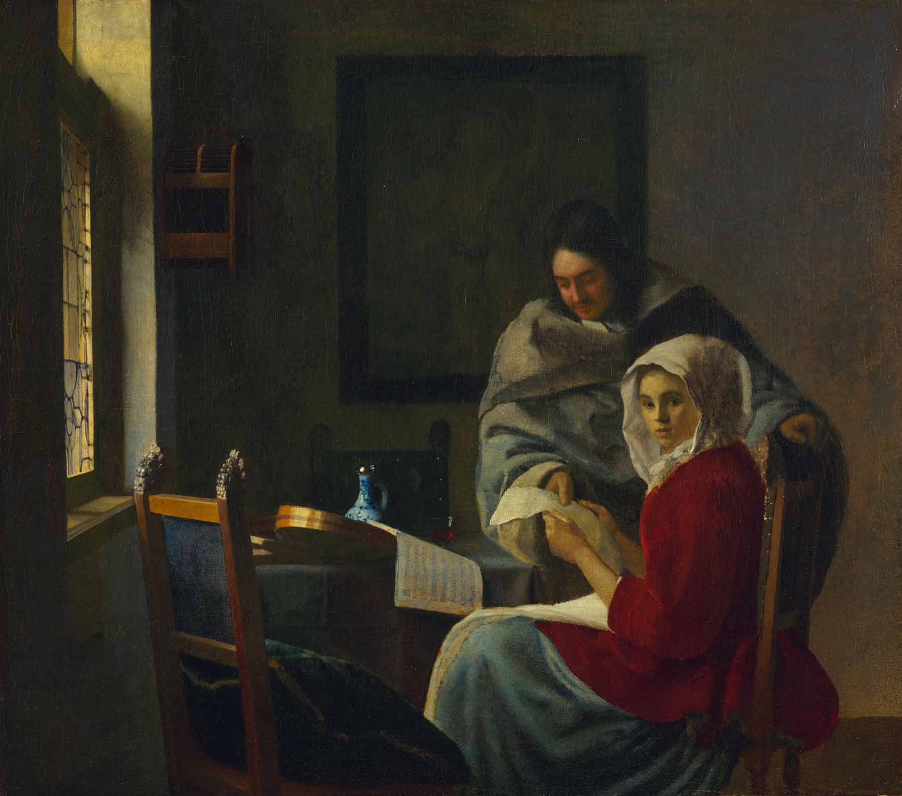 A man showing a paper to a woman in a headscarf seated at a table with a musical instrument and porcelain