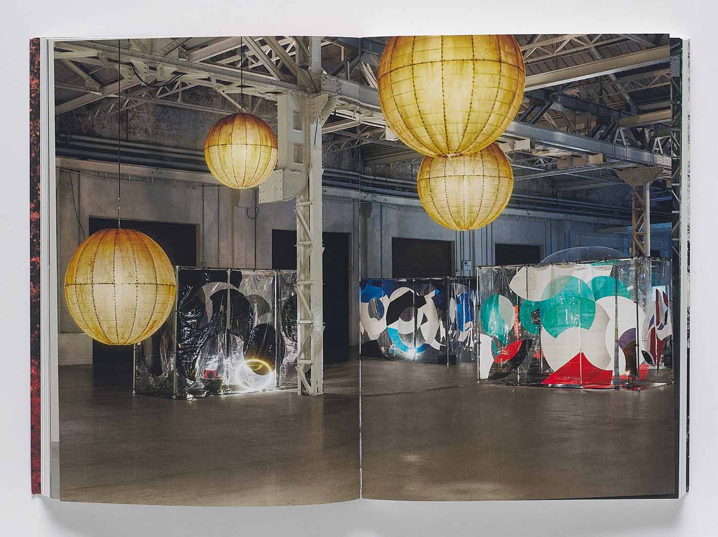 Book spread showing an art installation punctuated by four large yellow lanterns