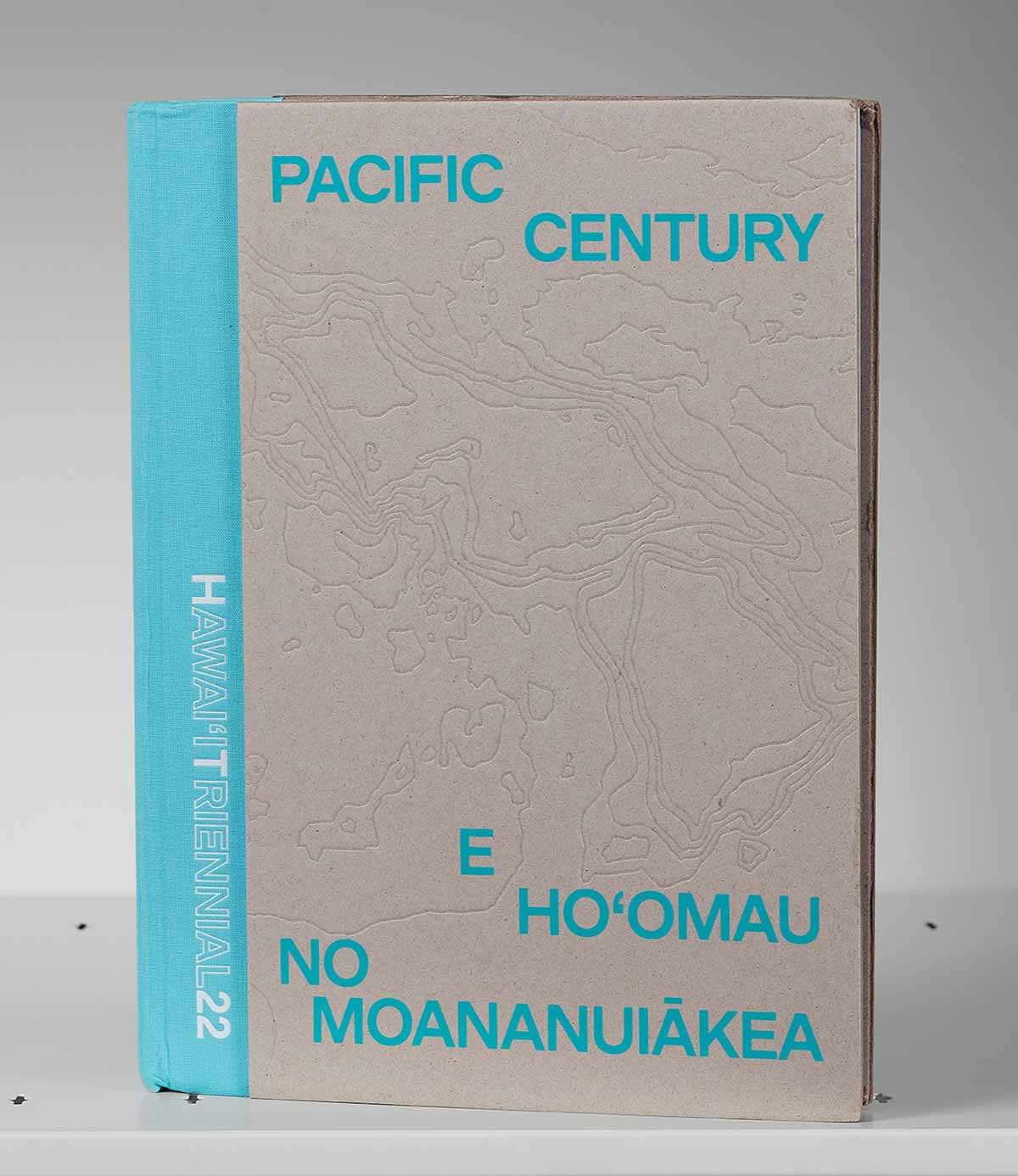 Gray book cover on a shelf with bright blue lettering and outlines of the Hawaiian islands