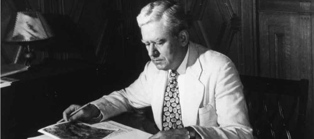 black and white photo of man seated at a desk over open papers