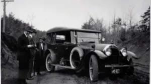Three people standing next to a car on a dirt road