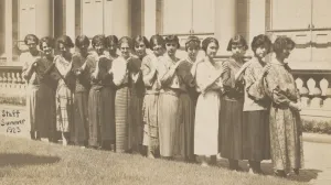 Fifteen women standing in a row in front of a building