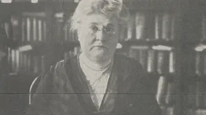 Detail from a newspaper clipping of a woman seated at a desk in front of large bookshelves