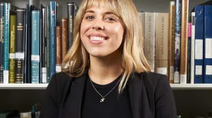 A blonde woman smiling in front of shelves filled with books