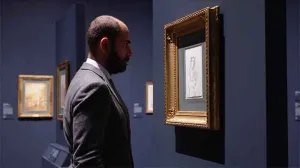 video still of Xavier F. Salomon looking closely at work in gallery