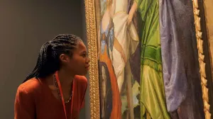 video still of woman looking closely at painting