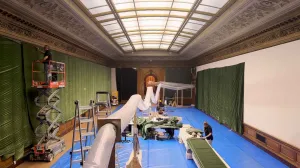 video still of West Gallery showing two figures, large green velvet tapestry and machinery and skylight
