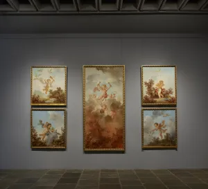 One tall canvas on a gray gallery wall flanked by four smaller canvases, each depicting a scene of flying cupids with doves, clouds, and flowers