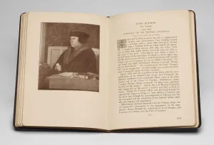 Book open to a spread with text on the right and an image of a seated man in a black hat and fur-lined coat on the left