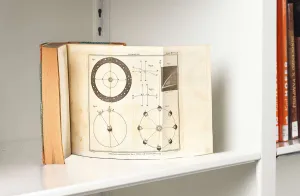 Book on a white shelf open to a page showing circular charts of planetary movement