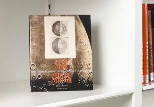Book on a white shelf whose cover features scientific sketches of the moon over a close-up photo of the lunar surface