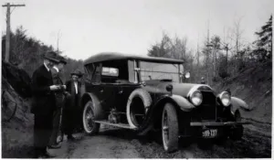 Three people standing next to a car on a dirt road