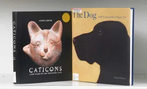 Two book covers on a white shelf, one featuring a painting of a dog and the other a sculpture of a cat
