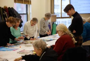 Man standing and overseeing a table of older women making collages