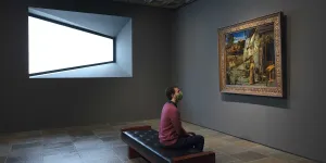 Man sitting between a window and Bellini's "St. Francis in the Desert"
