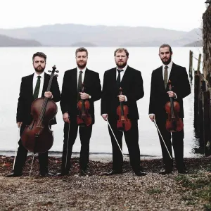four musicians holding instruments in front of body of water