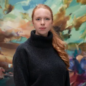 A woman in a black sweater standing in front of a multi-color mural