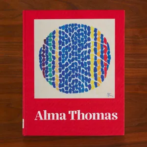 Red book cover with the title "Alma Thomas" and a circular abstract artwork with colorful splotches in lines