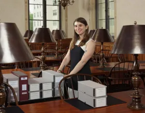 A woman in a library reading room pushing a cart of archival boxes