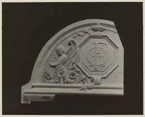Plaster model of half of a semicircular pediment carving featuring a monogram, a winged child pouring water, and leaves and flowers