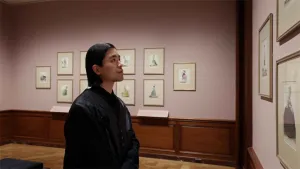 video still of person looking at prints in gallery