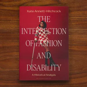 Book cover titled "The Intersection of Fashion and Disability" featuring a person posing in a red-and-white checked mini dress and boots using a cane