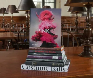 Stack of books on a wooden table, with one cover showing titled "Pink" featuring a figure swaddled in pink fabrics