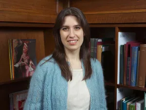 Woman with brown hair in a blue cardigan posing in front of a bookshelf