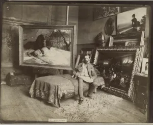 archival photo of, Gustave Wertheimer, the artist sitting on bed amongst large paintings