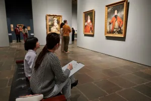 People sitting and standing in a room with portrait paintings