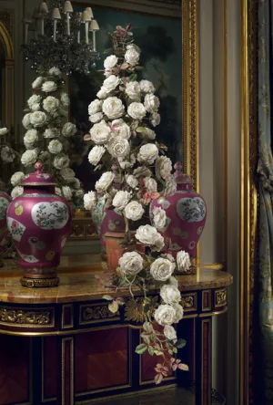 A pink vase filled with a sculpture of white roses