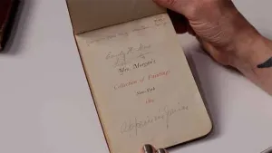 video still of woman's hand holding a catalog open, reads Mrs. Morgan's Collection of Paintings, New York, 1884