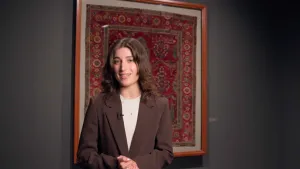 video still of woman standing in front of carpet on wall in gallery