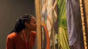 video still of woman looking closely at painting