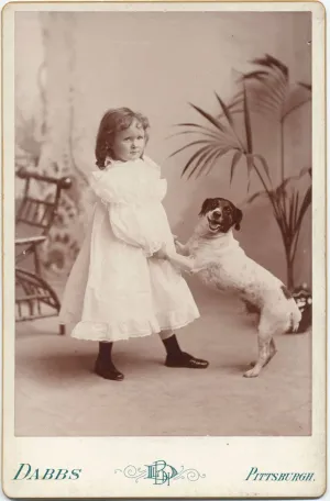 young Helen Clay Frick in dress holding front paws of dog, circa 1893