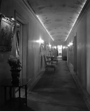 hallway with chairs, small tables, sconces, paintings