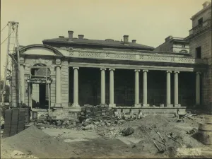 building with columns, scaffolding, bricks, dirt piles, men, shovels